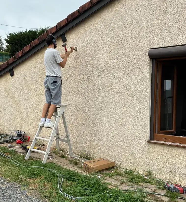 Technicien Clim Confort perçant le mur de façade pour le passage des liaisons frigorifiques d'une climatisation
